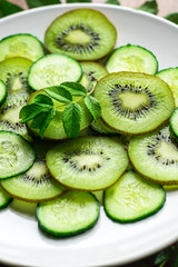 Close-up slices of kiwi and cucumber with leaf on white plate and rustic background