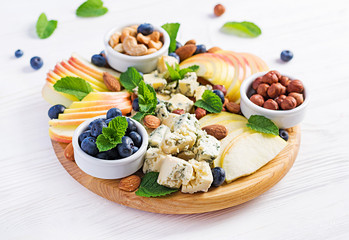 Cheese platter with assorted cheeses, blueberry, apples, nuts on white table. Italian cheese  platter and fruit.