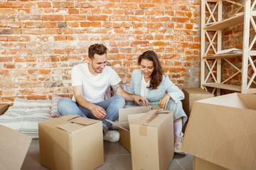 Young couple moved to a new house or apartment. Unpacking cardboard boxes together, having fun at moved day. Look happy, dreamful and confident. Family, moving, relations, first home concept.