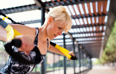 Fototapeta premium A young sportswoman doing exercise with TRX fitness straps outdoors.