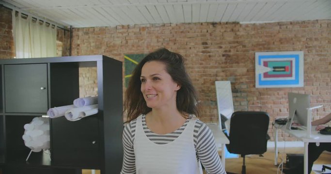 Young woman with graphs in folder jumps, looks happy with high growth rate and hugs colleagues
