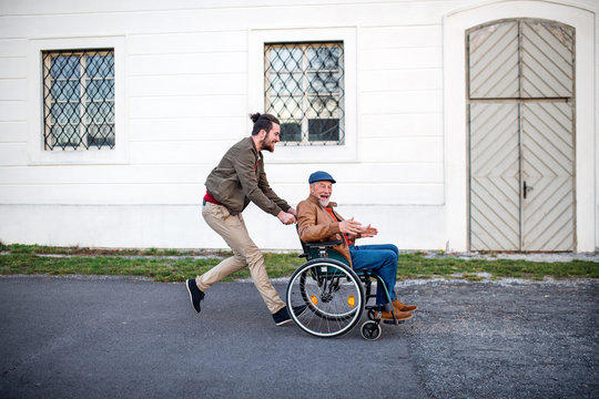 Young man and his senior father in wheelchair on a walk in town, having fun.
