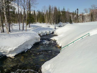 A small river in a snowy winter forest on a sunny day.