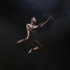 Naked muscled male jumping and raising hands