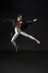 Fototapeta na wymiar Young man in stylish clothes jumping and dancing on black background