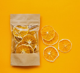 Healthy snack. Fruit chips from organic oranges in a paper bag on a bright orange background and a few circles of chips nearby.
