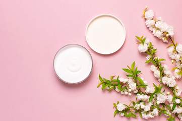 Obraz na płótnie Canvas Beauty Spa concept. Opened plastic container with cream and spring White flowers on pink background Flat lay top view. Herbal dermatology cosmetic hygienic cream, organic cosmetic Natural