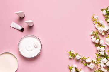 Beauty Spa concept. Opened plastic container with cream, cosmetic bottle containers, spring White flowers on pink background Flat lay top view. Herbal dermatology cosmetic hygienic cream organic