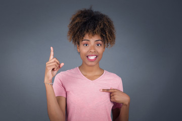 Positive glad female says: wow how exciting it is, has amazed expression, indicates something. Joyful pretty young woman demonstrates something. One hand on her chest and pointing with other hand.