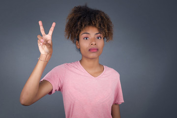 Young African American woman standing against gray wall showing and pointing up with fingers number two while smiling confident and happy.