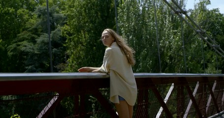 sexy slender lady is standing on bridge in city in sunny day, back view