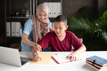 The muslim woman teaching young boy for writing report,two students doing activity together,at school,blurry light around