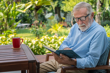 Senior elderly man reading book with mug of coffee in garden