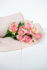Pink roses laying on a thick knit woolen cosy blanket laying on a white wooden background 