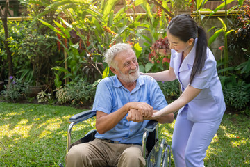 Happy nurse holding elderly man hand on wheelchair in garden at nursing home