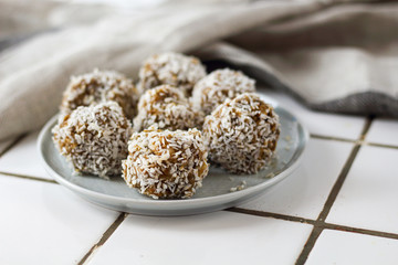 vegetarian raw healthy diet  no bake candies balls dessert sweets sugar free gluten-free with coconut flakes, proper nutrition snack on blue plate on a white tile background, soft selective focus