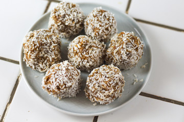 vegetarian raw healthy diet  no bake candies balls dessert sweets sugar free gluten-free with coconut flakes, proper nutrition snack on blue plate on a white tile background, soft selective focus