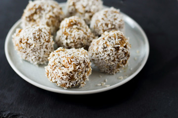 vegetarian raw healthy diet  no bake candies balls dessert sweets sugar free gluten-free with coconut flakes, proper nutrition snack on blue plate and black slate background, soft selective focus