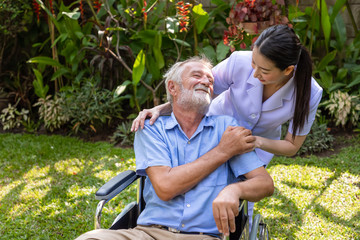 Naklejka na ściany i meble Happy nurse take care elderly man on wheelchair in garden at nursing home