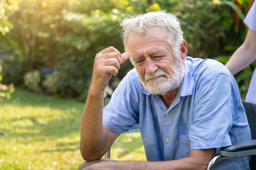 Depressed thoughtful elderly man on wheelchair with nurse in garden at nursing home