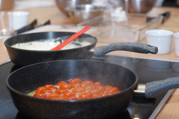 Two pans on the stove, in one cherry tomatoes, in another white sauce, steam comes from heating