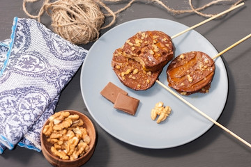 Slices of apples in chocolate, caramel glaze and walnuts on skewers on a dark background