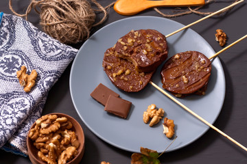 Slices of apples in chocolate, caramel glaze and walnuts on skewers on a dark background