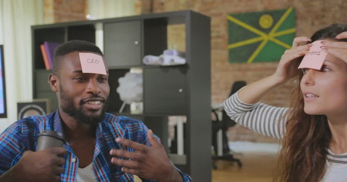 Young colleagues play in team bulding game. Black guy tries to guess what is written on sticky note