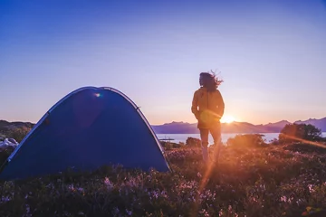 Crédence de cuisine en verre imprimé Reinefjorden Traveler girl in a yellow jacket stands next to a tent in Norway at sunset