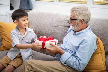 Obraz premium Happy boy grandson playing with old senior man grandfather at home with present