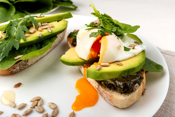 Breakfast. Bread toasts with poached egg and avocado with spinach, fresh arugula and seeds