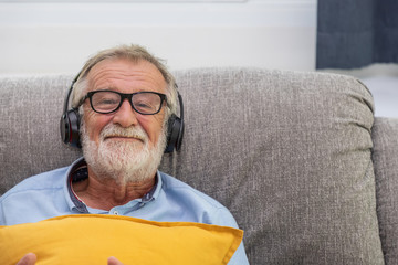 Senior old man eldery enjoy listening to music with headphone on couch sofa looking camera