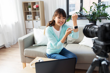 blogging, technology and videoblog concept - happy smiling asian woman or blogger with camera recording video blog of smart watch at home