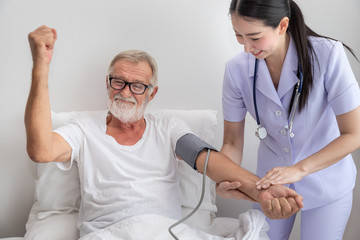 Obraz premium Happy nurse checking and measuring elderly man blood pressure in bedroom at nursing home, rise fist up
