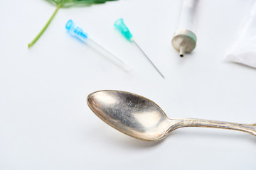 close up view of spoon, syringe and needles on white background