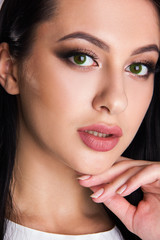 Fototapeta na wymiar Close-up portrait of sensuality young brunette girl with green eyes, woman with stylish make up is looking straight and posing cute with hand near her face, beauty concept