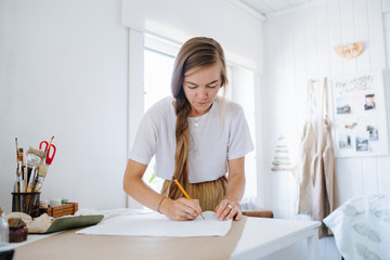 Young woman artist drawing on sheet, behind the table at home.