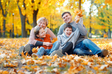 Happy family sitting on fallen leaves, playing and having fun in autumn city park. Children and parents together having a nice day. Bright sunlight and yellow leaves on trees, fall season.