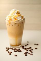 Ice coffee in the glass topped whipping cream with coffee beans. Cold summer drink on wooden background and copy space. Advertising for caramel mocha and chocolate beverage for the cafe.
