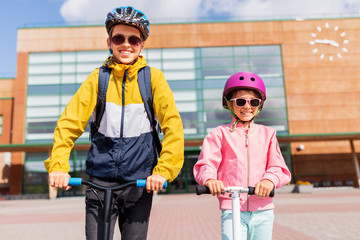 education, childhood and people concept - happy school children in helmets with backpacks riding scooters outdoors © Syda Productions