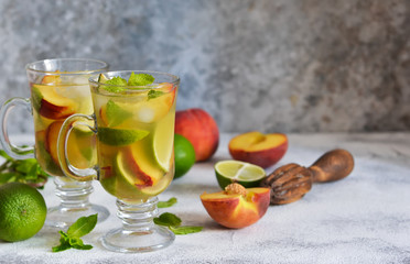 Cold summer drink with peach, lime and mint on a concrete background.