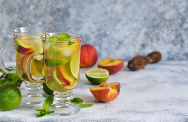 Cold summer drink with peach, lime and mint on a concrete background.
