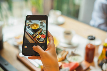 Woman taking photo on cellphone on dish. Woman taking photo of food with mobile phone in morning.