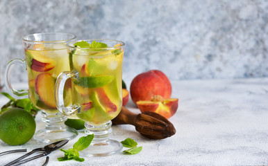 Cold summer drink with peach, lime and mint on a concrete background.