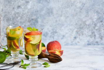 Cold summer drink with peach, lime and mint on a concrete background.