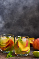 Cold lemonade with peach and lime on a dark concrete background.