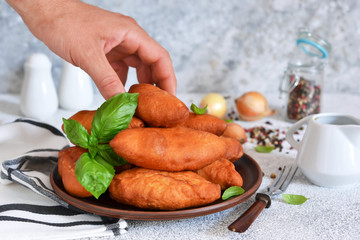 Fat pies with meat and onions in a plate on the kitchen table.