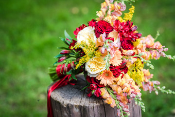 Boho wedding bouquet made of red and yellow mixed flowers on the green grass.