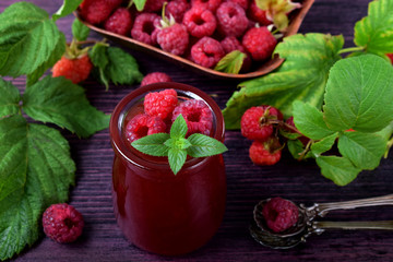 Raspberry jam in glass jar topped with berries and mint