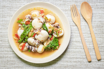Stir fried Cuttlefish or Cuttlefish Rainbow with basil on table mat with wooden spoon and fork; top view. Thailand's popular dishes (Pad Ga Pow).